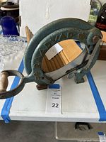 Front angled view showing blue painted iron frame with handle and slicing blade inside semicircular frame, wooden base visible.