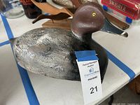 Photo showing a vintage painted wooden duck decoy with dark brown head, yellow eyes, and textured grayish body.