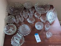 Full assortment of 26 pieces including bowls of various sizes, round butter dish with lid, hexagonal candleholders, and other glassware pieces on wooden table.
