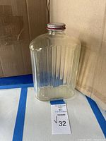 Full view of clear ribbed glass bottle standing upright with red metal lid, showing vertical ribbed texture and rounded edges.