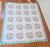 Full view of vintage Dresden Plate patterned quilt laid flat, showing pastel pink and green circular motifs and scalloped edges.