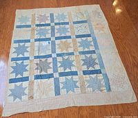 Full view of the vintage handmade star pattern patchwork quilt laid flat on floor, showing overall condition and pattern in blue, beige, pink, and cream tones.