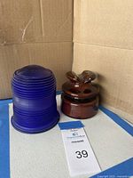 Vintage ceramic insulator next to cobalt blue ribbed glass light cover inside cardboard box.