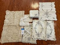 Full view of all table linens arranged on wooden floor, showing lace tablecloth, table runners, and napkins.