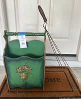 Front view of green wooden magazine holder with floral design and attached label visible.