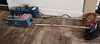 Side view of two vintage metal detectors laid on wooden floor, showing metal coils and control boxes.