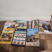 Shows a group of magazines and instructional manuals for model trains arranged on the floor. Titles visible include Classic Toy Trains, Model Railroading, and instructional booklets on HO scale railroad structures and scenery techniques.