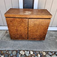 Front view of rectangular burl wood server cabinet showing two doors with natural wood grain pattern and worn top surface.