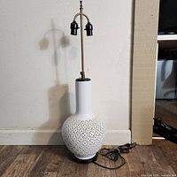 White porcelain lamp base with pierced floral lattice pattern and brass fittings, unplugged with cord visible