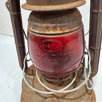 Close-up of red glass globe with embossed 'DIETZ Little Wizard N.Y. U.S.A.' showing wear and rust on metal parts.