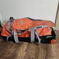 Side view of large orange Eastern Mountain Sports wheeled duffle bag showing logo and wheels