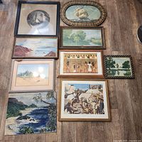 Nine framed artworks arranged on floor including dog portrait, ship, landscapes, Egyptian and Mayan scenes