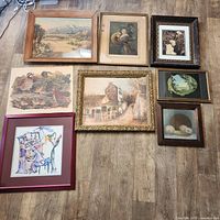 Overview of 8 framed art pieces arranged on wood floor including nature scenes, a jazz pianist, mother and child, and still life.