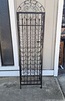 Full view of tall wrought iron wine rack with multiple bottle slots and decorative arch