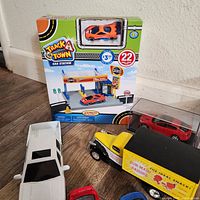 Lot showing Track A Town Gas Station playset with orange sports car and several diecast vehicles including white SUV, yellow vintage truck with Sun-Maid Raisins box, and red, blue, and black diecast cars
