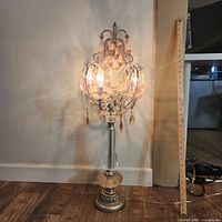 Full view of the lit mid century pink chandelier table lamp with measuring stick beside it showing height and wooden floor background.