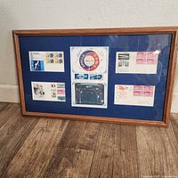 Framed collection with six first day covers and stamps arranged inside a wooden frame with blue matte