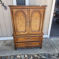 Front view of the vintage Drexel Cabernet armoire showing detailed wood panels on cabinet doors, two drawers below, and ornate handles.
