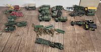 Overview of multiple vintage military diecast vehicles and loose green plastic army men accessories spread on wooden floor.