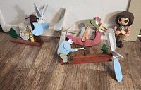 Photo showing three wooden whirligig figures in various poses with propellers and swinging arms on wooden bases on a wood floor.