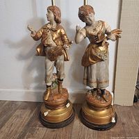 Pair of Marbro figurine lamps showing young male and female figurines in period clothing on round bases.