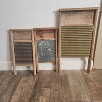 Three vintage wooden washboards of varying sizes seen leaning against a wall on a wood floor.
