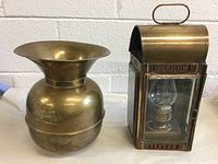 Two brass antique items: Union Pacific Railroad spittoon and brass carriage lamp shown side by side on table against white brick wall.