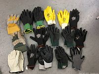 Top-down view showing all 20 assorted gloves in various styles and colors arranged on a gray concrete floor.