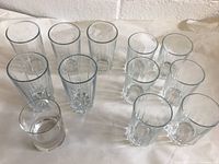 Lot of 13 glasses arranged on a surface: 7 taller highball glasses and 6 shorter lowball glasses.