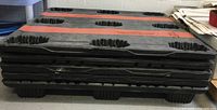 Stacked black plastic skids with orange safety strips visible along their length.
