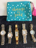 Top view of the five wristwatches laid out horizontally with a teal pouch labeled 'change is good' above them.