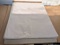 Stack of flat white newsprint sheets in an open cardboard box viewed from top angle, showing the size and condition of sheets.