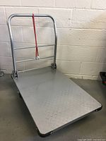 Full view of the steel platform cart showing the deck and large tubular handle with red elastic strap.