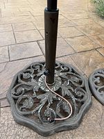 Close up of larger patio umbrella stand base with ornate floral pattern and central pole with 2-inch diameter. Surface shows wear and some rust.