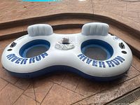 Top down view of the gray and blue inflatable 2 person river tube showing two blue circular seats labeled 'RIVER RUN' with headrests and a center cooler section.