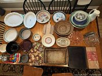 Overview photo of all kitchenware and bakeware items on a table including plates, bowls, trays, carafe, cutting boards, place mats, and measuring spoons