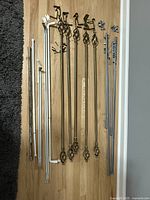 Full assortment of approx. 12 metal curtain rods and brackets on wood floor showing variety of sizes, colors, and styles.
