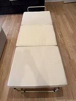 Beige ottoman fully unfolded into a fold-out twin bed showing foam mattress sections and metal frame