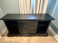 Front view of the black painted wood sideboard showing three drawers in the middle and two open shelf spaces on each side. Top surface and base visible with minor wear.