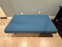 Top view of the futon sofa bed in bed form, showing the blue fabric upholstery and metal legs underneath.