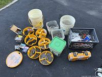 Wide view of entire lot showing multiple yellow compartmentalized organizers, white buckets, bins, and boxes of screws and nails on asphalt surface.