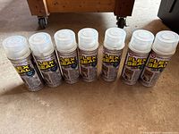 Seven Flex Seal clear spray cans in an upright row on the floor, showing brand and cap details.
