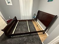Disassembled full size dark cherry sleigh bed frame assembled and laid out on floor showing headboard, footboard, side rails, and support beams