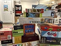 Stacked board games and various puzzles with visible titles including Funny Animals 1000 piece puzzle, MAD GAB, ReaLies, Gotcha, and others.