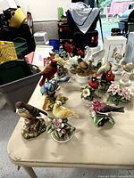 Photo of bird figurines in varied colors including cardinals, blue birds, yellow birds, and floral bases on a table.