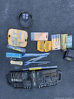 Photo showing plastic cases and packages with various drill bits and accessories laid out on black surface.