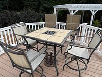 Full view of outdoor high-top patio dining set on deck, showing metal frame table with tile top and five swivel chairs with mesh sling seats.