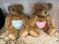 Pair of brown Vermont Teddy Bears shown sitting on a countertop, each wearing a cloth diaper, photo captures both bears.