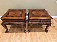 Pair of wooden end tables with multitone inlay tops, visible carved legs and aprons, medium to dark brown finish, placed on hardwood floor against wall.
