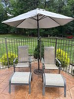 Full view of the patio set including two chairs, two ottomans, and one umbrella with stand on outdoor patio